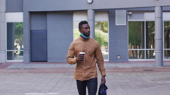 African american businessman with face mask drinking coffee in street