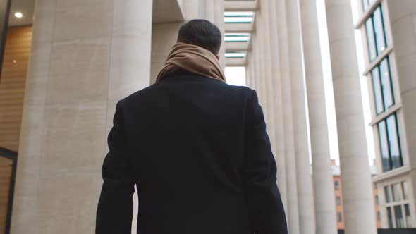 Back View of Businessman in Coat and Scarf Walking Outdoors Along Street