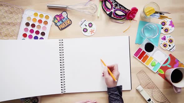 Step by step. Flat lay. Baker sketching a design of a cake for Dia de los Muertos holiday.