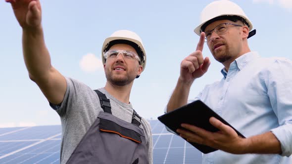 Two Workers in Helmets Check the Installed Solar Panels