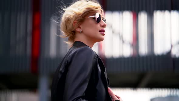 Portrait of a Blonde Woman in Dark Glasses and a Black Leather Jacket in Profile. She Goes Against