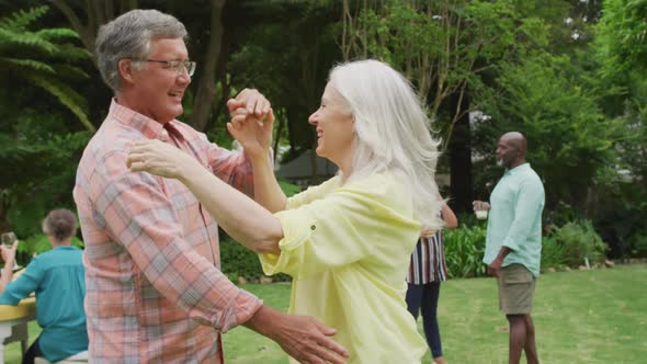 Animation of happy caucasian senior couple danging in garden while having lunch with friends