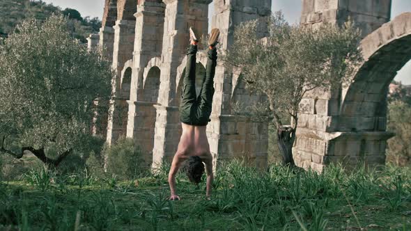 Young man performs one handstand push-up outdoors in front of ancient aqueduct