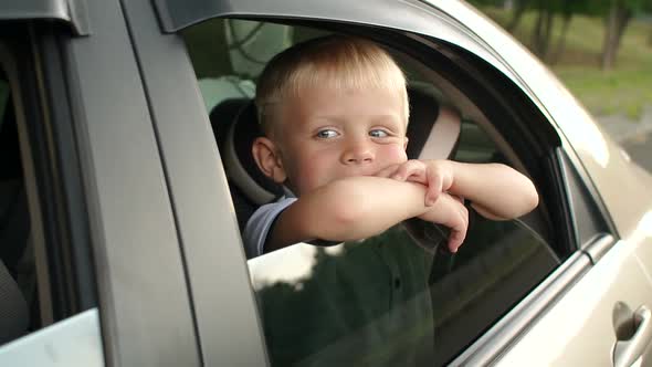 A Little Boy Sits in the Backseat of a Car He Looks Out the Window and Smiles