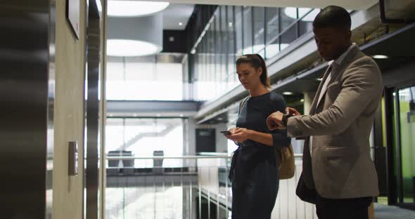 Diverse businessman and businesswoman waiting for lift and arriving in modern office