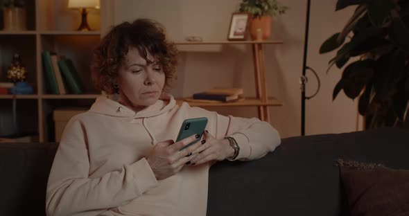 Close Up of Amazed Woman with Short Curly Hair Scrolling Phone Screen While Sitting on Couch at Home