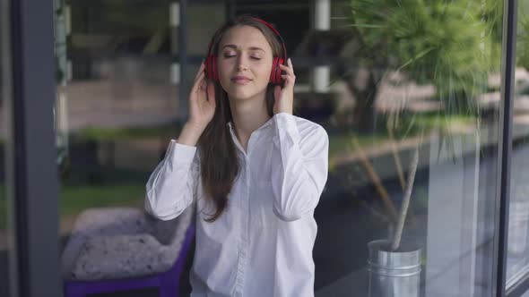 Medium Shot Happy Carefree Millennial Caucasian Woman Listening to Music in Headphones Standing in