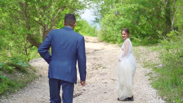 Cheerful and Happy Newlyweds Walk Along a Mountain Path Among the Trees