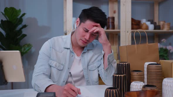 Depressed Asian male look frustrated to sale order in book and think of financial problem at store.