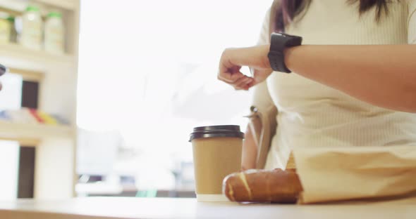 Video of hands of biracial woman paying with smartwatch for coffee
