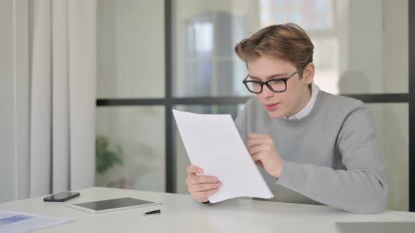 Young Man Feeling Happy While Reading Documents in Modern Office