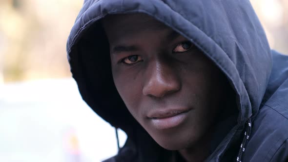 Thoughtful confident hooded young black african migrant looking at camera in the street