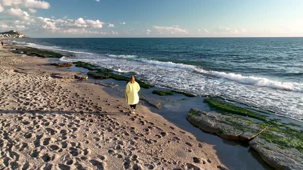 A girl in a yellow coat walks on the beach 4 K Aerial View