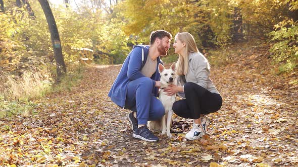 Young Couple Dressed in Sports Clothes Hugging and Kissing in Autumn Park, They Are Walking Their