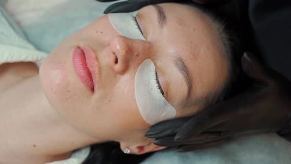 Eyelash Extension Master in Black Gloves Sticks Protective Patches Under the Client's Eyes Before