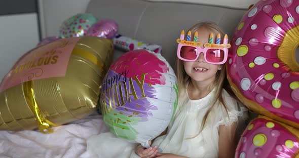 Happy little girl celebrating birthday at home with foil balloons