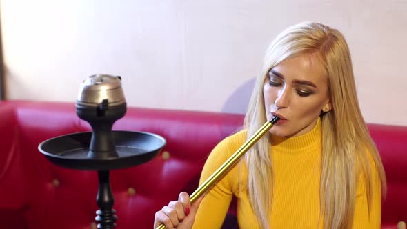 Pretty Woman in a Bright Yellow Sweaters Resting in a Bar and Smokes a Hookah.