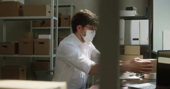 Man Employee of Warehouse Wearing Medical Mask Taking Delivery Box and Writing Information About