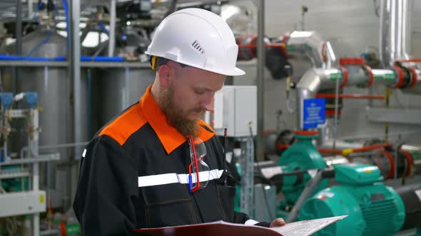 An Industrial Engineer in a White Helmet Conducts an Inspection at His Workplace Uses a Folder with