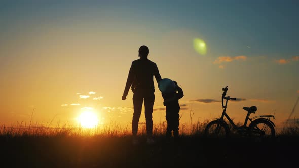 Silhouette of Mother Teaching Little Son to Ride a Bike at Meadow During Sunset