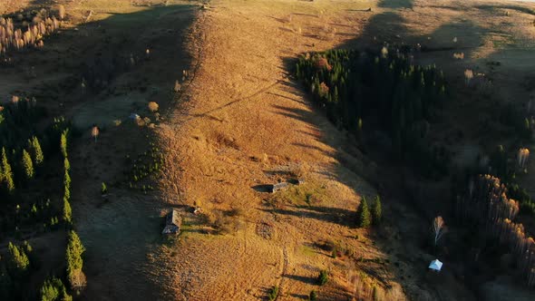 Flight Over a Mountain Ridge at Sunset or Sunrise with Golden Light and Forested Slopes - Aerial