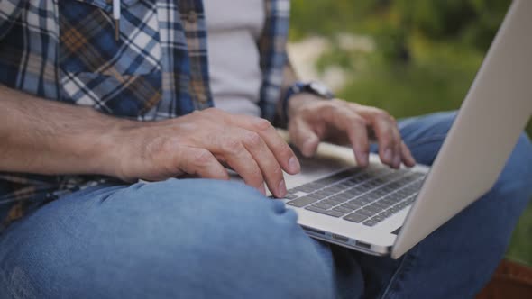 Closeup of the Hands of a Middleaged Man Working on a Laptop in an Outdoor Park