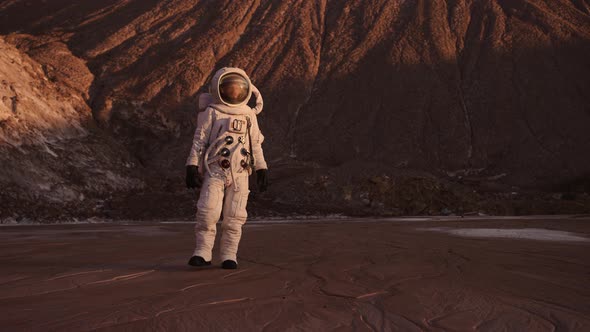 Astronaut Steps Away From the Cliff Raises His Hand Up Closing From Bright Sun