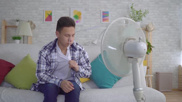 Young Asian Man Sitting in Front of a Working Fan the Concept of Heat