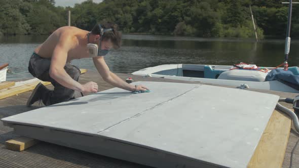 Young shirtless man wiping down plywood engine cover with acetone before painting