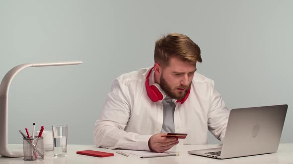 Young Man Sits at Laptop in His Home Office and Makes Online Shopping Using Bank Card