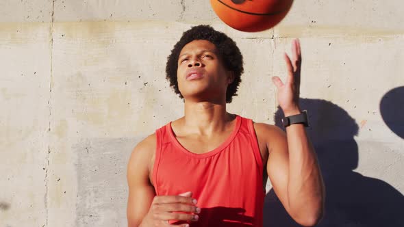 Fit african american man exercising outdoors in city, playing with basketball