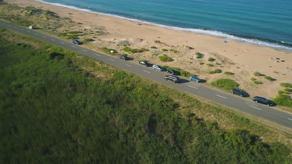 Drone Following Car Driving at Asphalt Coast Road. Sand Beach and Clear Blue Sea Water