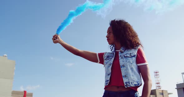 Fashionable young woman on urban rooftop using a smoke grenade