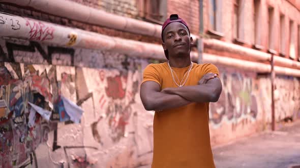 A young black guy poses in an alley that is covered with graffiti on the walls