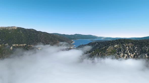 Drone flies above the clouds filming Big Bear Lake between mountains in California, USA