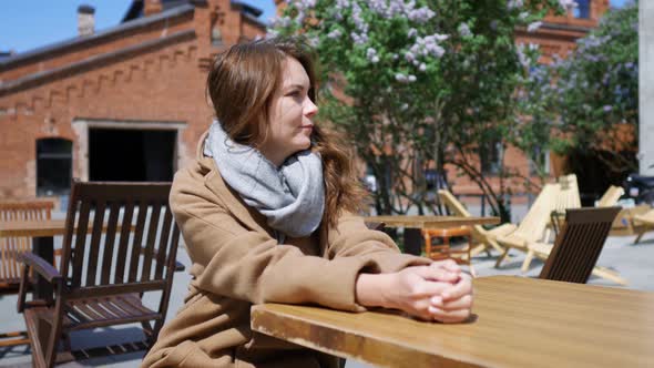 charming woman is waiting at a table of a street cafe