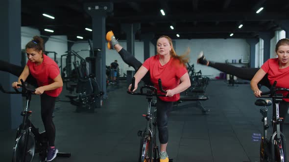 Group Athletic Girls Performing Aerobic Ride Training Exercises on Cycle Stationary Bike in Gym