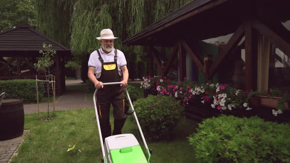 Elder Man Using Lawn Mower While Young Girl Cutting Bushes