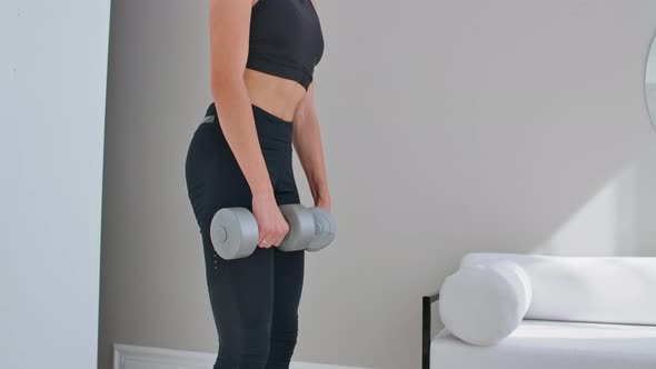 A Young Athletic Woman in a Bright Apartment Performs a Deadlift with Dumbbells at Home Making Leans
