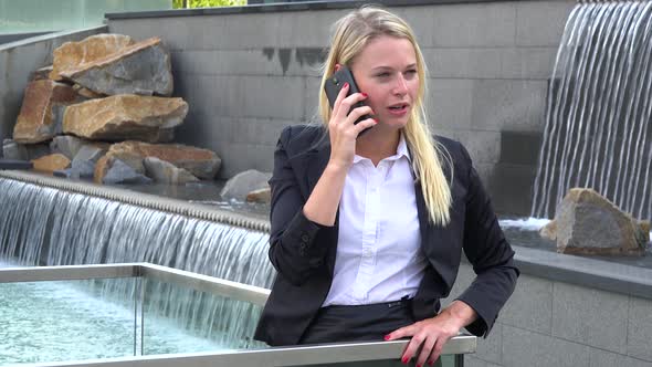 A Young Beautiful Businesswoman Talks on a Smartphone in an Urban Area - Artificial Waterfalls