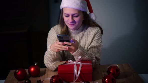 Young Beautiful Woman in Christmas Hat Looking to the Smartphone Screen