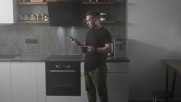 Young Man in His Kitchen with a Smartphone in His Hand