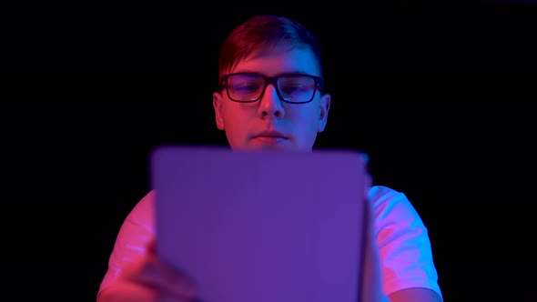 Young Man with a Tablet. A Man Is Using a Tablet. Blue and Red Light Falls on a Man on a Black