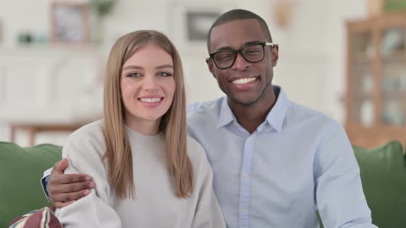 Embracing Mixed Race Couple Smiling at Camera While Sitting on Sofa