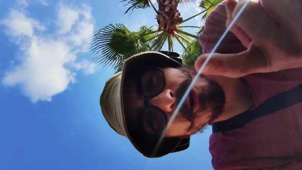 A Man Walking on Touristic Warm Town Found Camera and Starts Talking with Palm Tree on Background