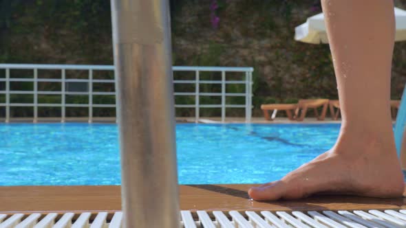 A Girl with Bare Feet Is Walking Along the Edge of a Pool of Blue Clear Water.