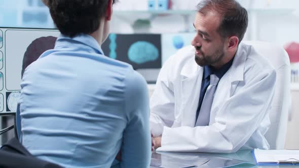 Over the Shoulder Shot of Medical Scientist Showing To Patient a 3D Brain Simulation