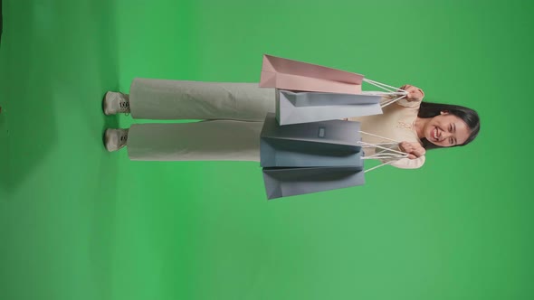 Full View Of Woman Holding Shopping Bags Up Smile To Camera While Standing In Front Of Green Screen