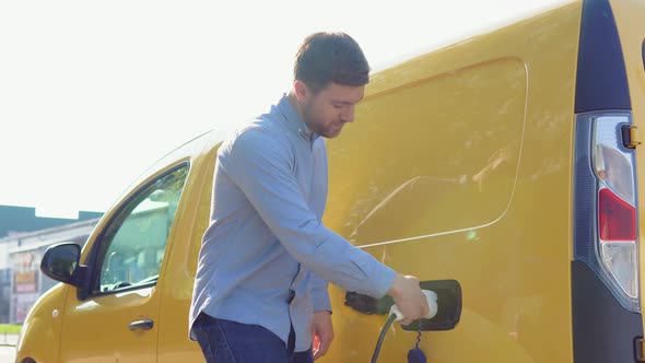 A Man Plugging in Charging Cable to to Electric Vehicle and Charges Batteries