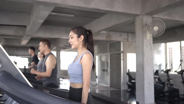 4K Group of Asian man and woman jogging on treadmill together at fitness gym.